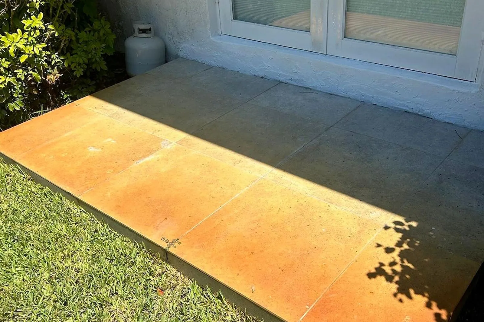 A concrete slab stained orange by sprinkler rust, before and after treatment — before
