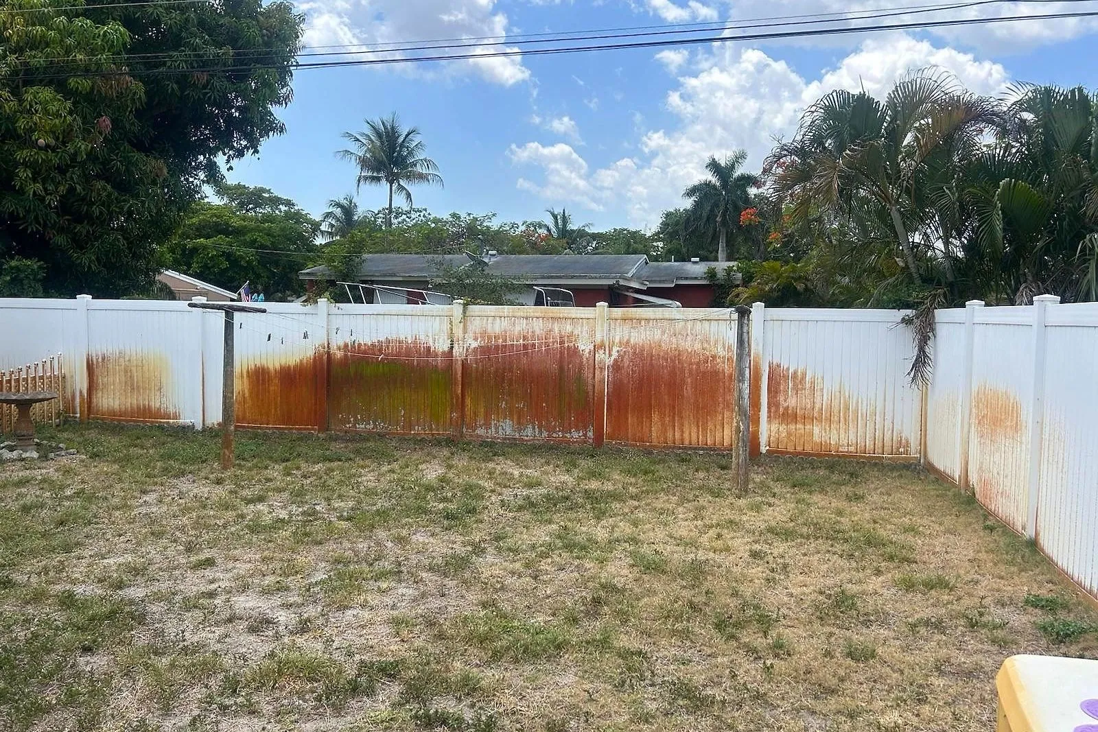 A white vinyl fence stained orange with sprinkler rust, before and after treatment — before