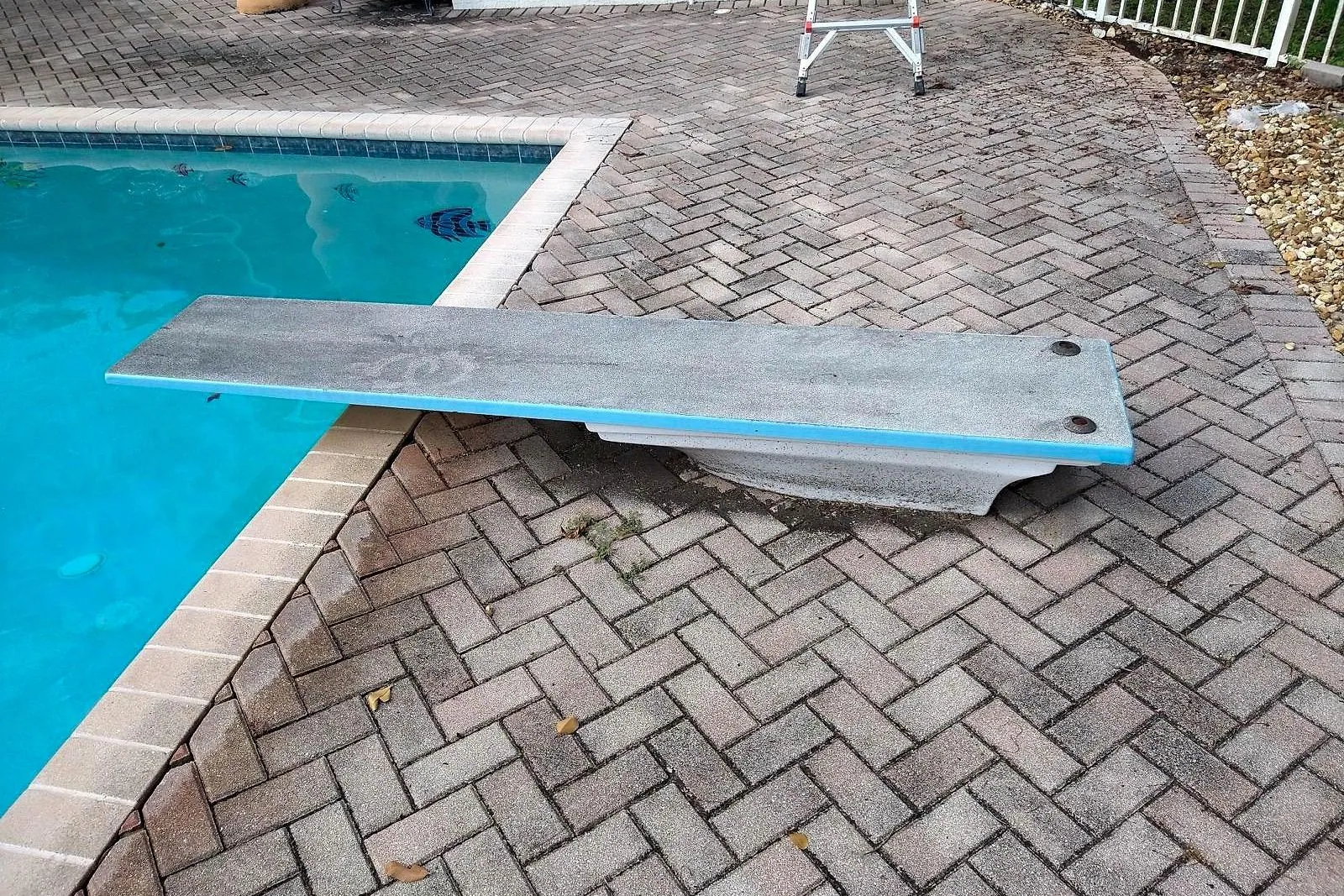 A paver pool deck with a diving board before and after cleaning — before