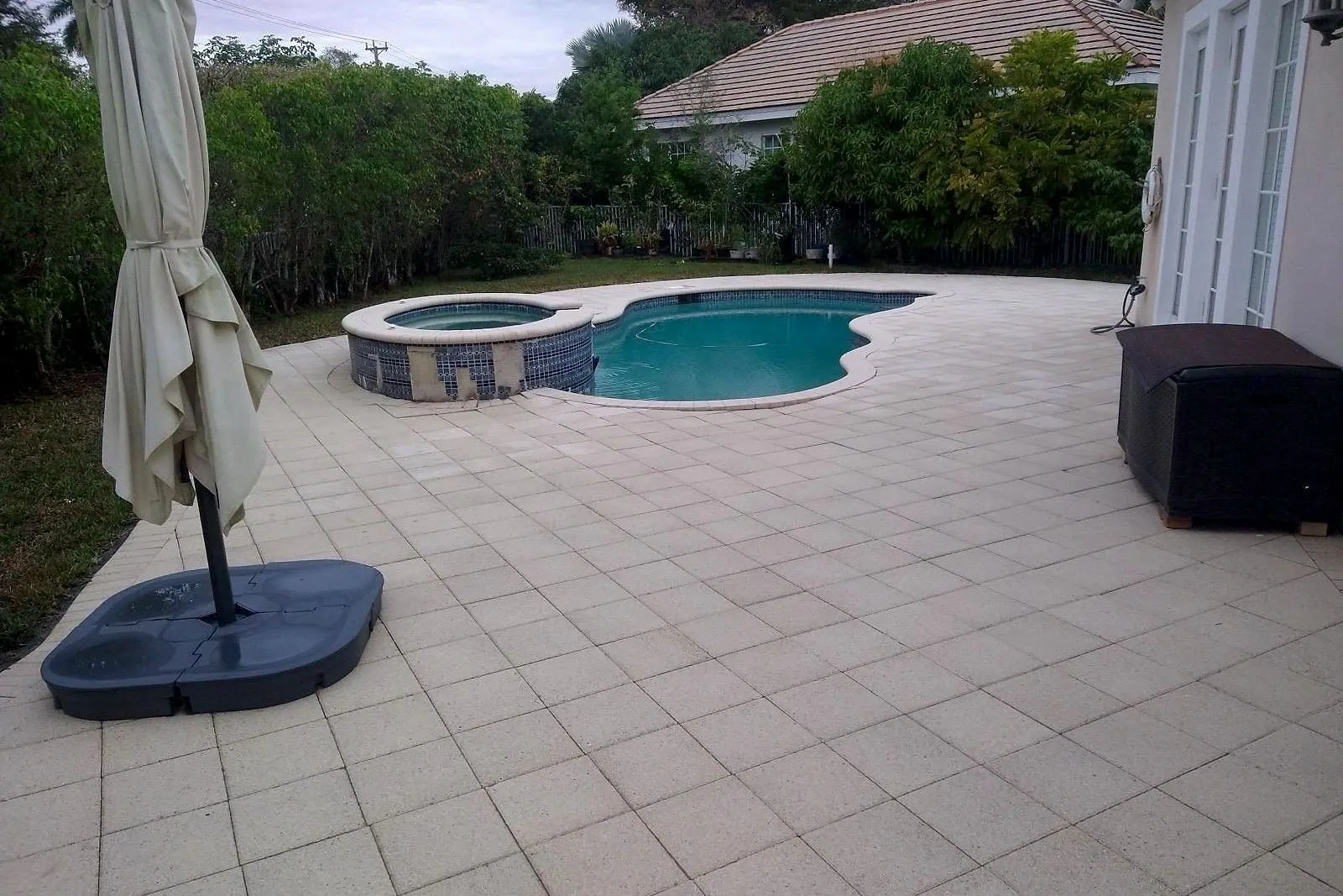 A tiled pool deck before and after cleaning, with the pool and spa in frame — after